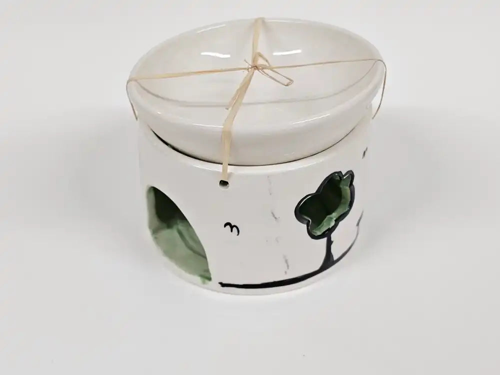 A white ceramic dog toy or chew holder with a matching lid, decorated with a green clover and black line art, tied with a string.