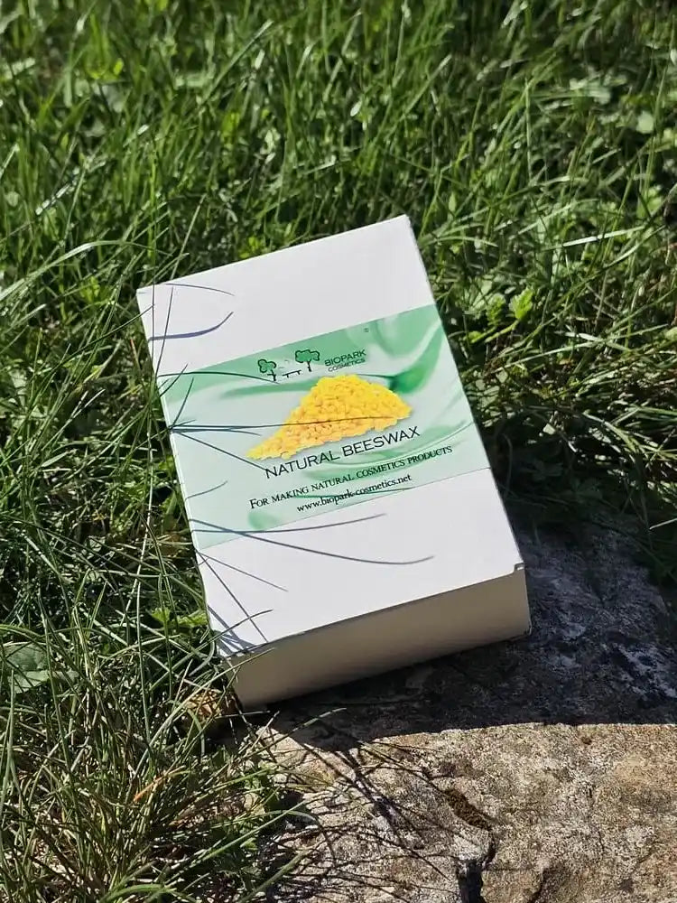 A white box of natural beeswax candles with a green and yellow label, placed on a patch of green grass and stone outdoors.