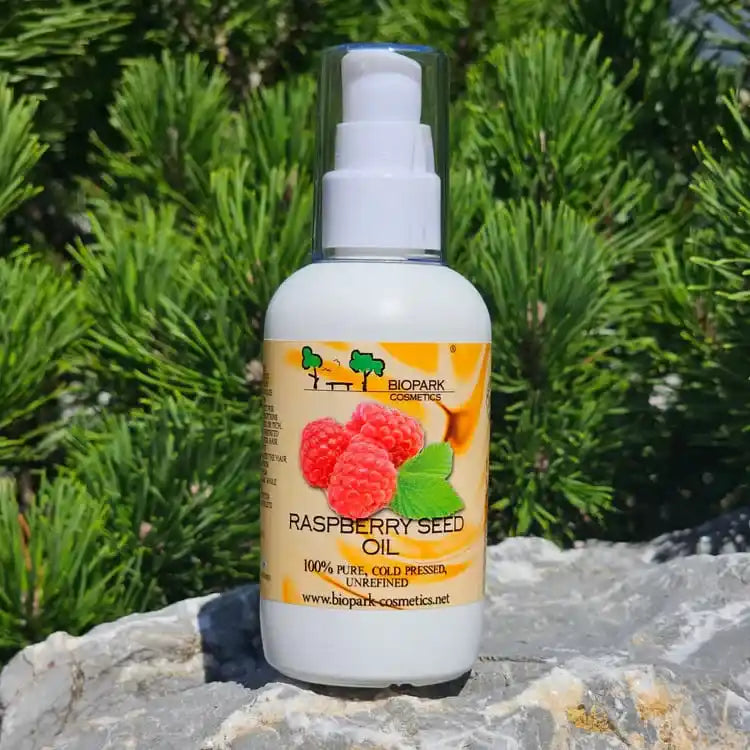 A bottle of Biopark Cosmetics Raspberry Seed Oil placed on a gray stone with green pine foliage in the background.
