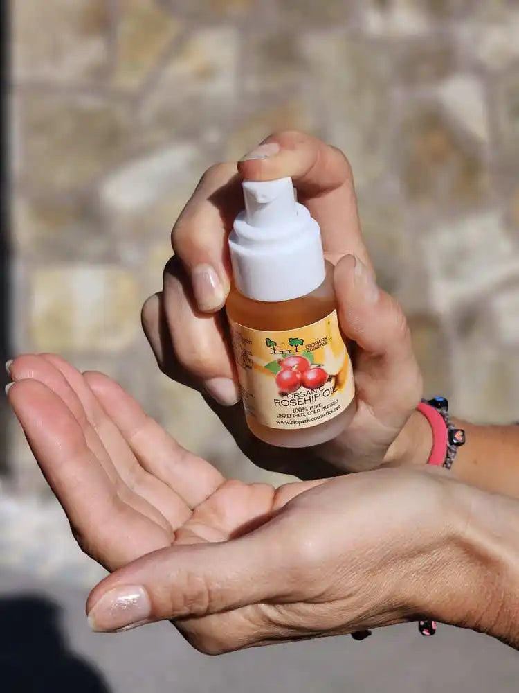 A person's hands holding a small bottle of cherry blossom hair growth oil over their open palm, with a blurred stone wall in the background.