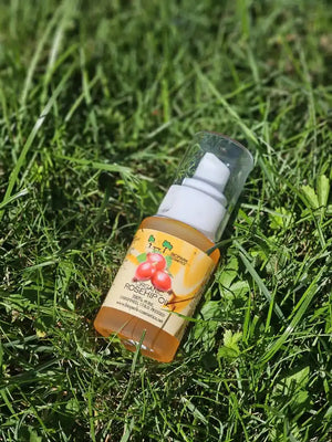 A bottle of Rosehip Oil by The Beauty Brand, lying on a green grass background.