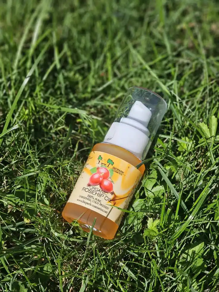 A bottle of Rosehip Oil by The Beauty Brand, lying on a green grass background.