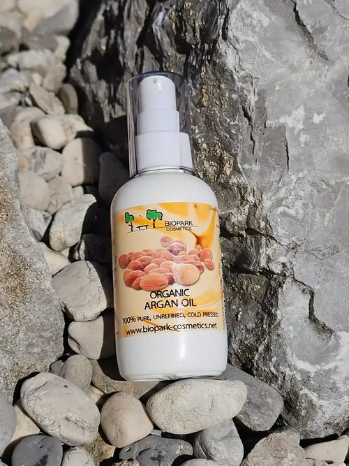 A bottle of BioPark Cosmetics Organic Argan Oil, placed on smooth gray stones against a larger rock background.