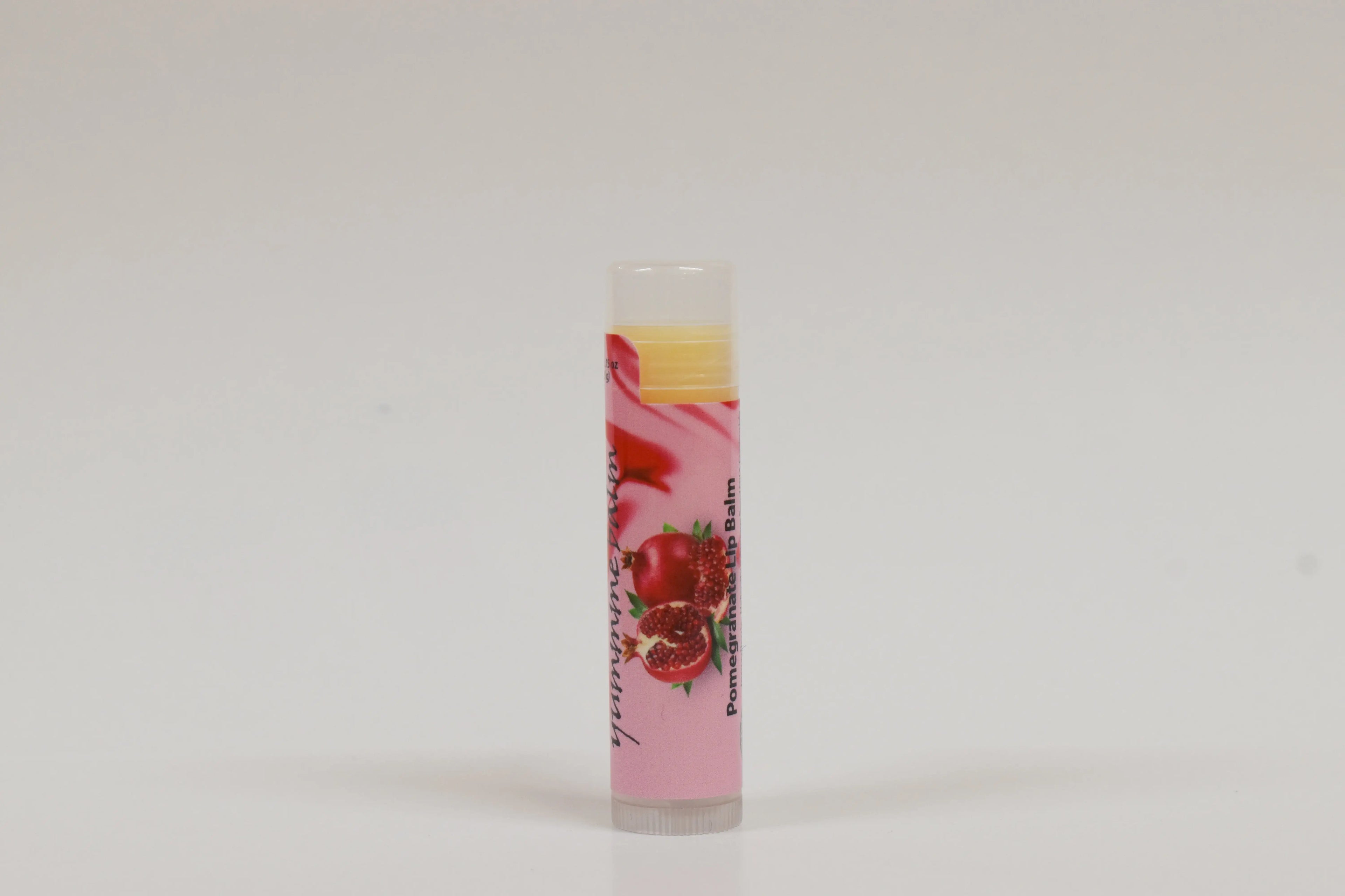 Lip balm with a pink label featuring pomegranate graphics on a white background