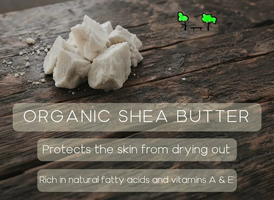 Raw chunks of off-white organic shea butter displayed on a dark rustic wooden surface, with text overlays describing its benefits and a small green logo in the top right.